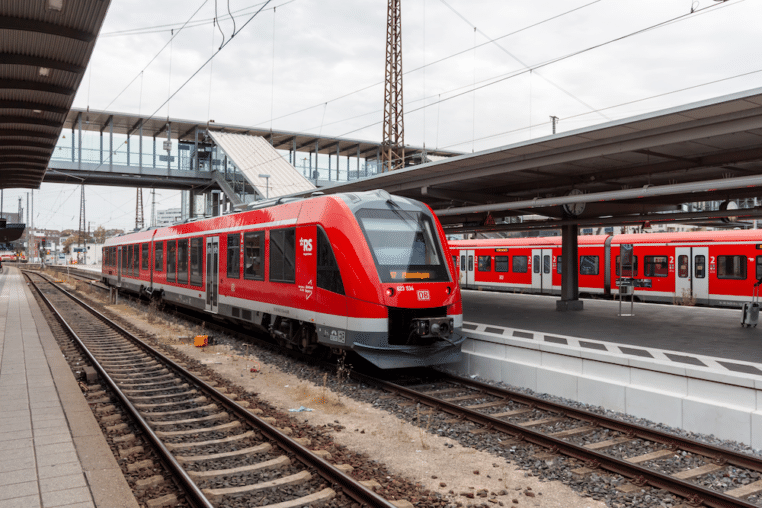 Roter Regionalzug der Deutschen Bahn am Bahnhof Ulm mit überdachten Bahnsteigen und Oberleitungen.